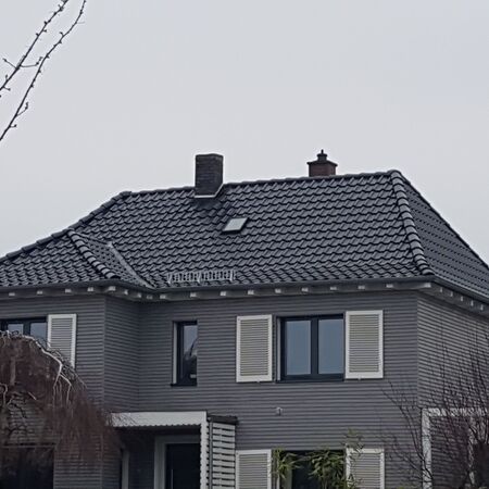 Neu eingedecktes schwarzes Dach auf einem Haus mit grauer Fassade und weißen Fensterläden