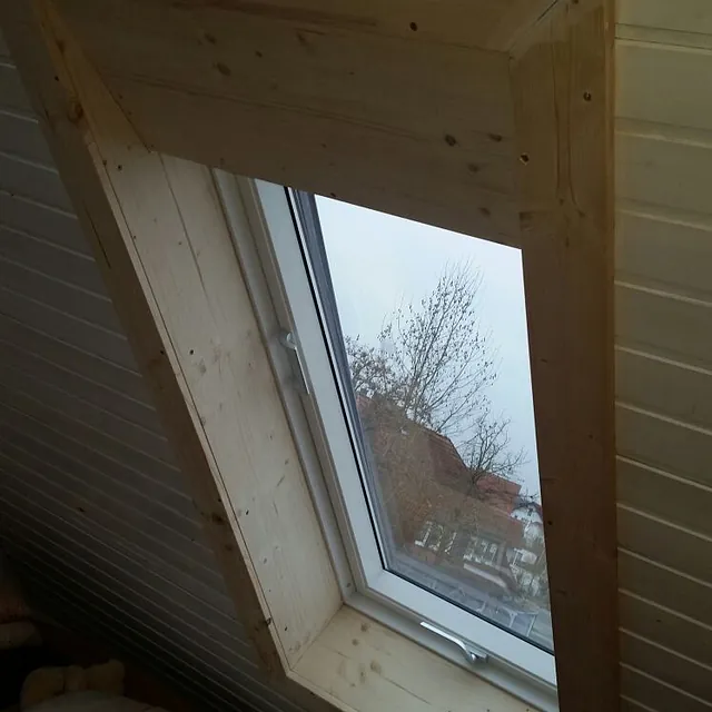 Neu eingebautes Dachfenster in einer mit hellem Holz verkleideten Dachschrägen